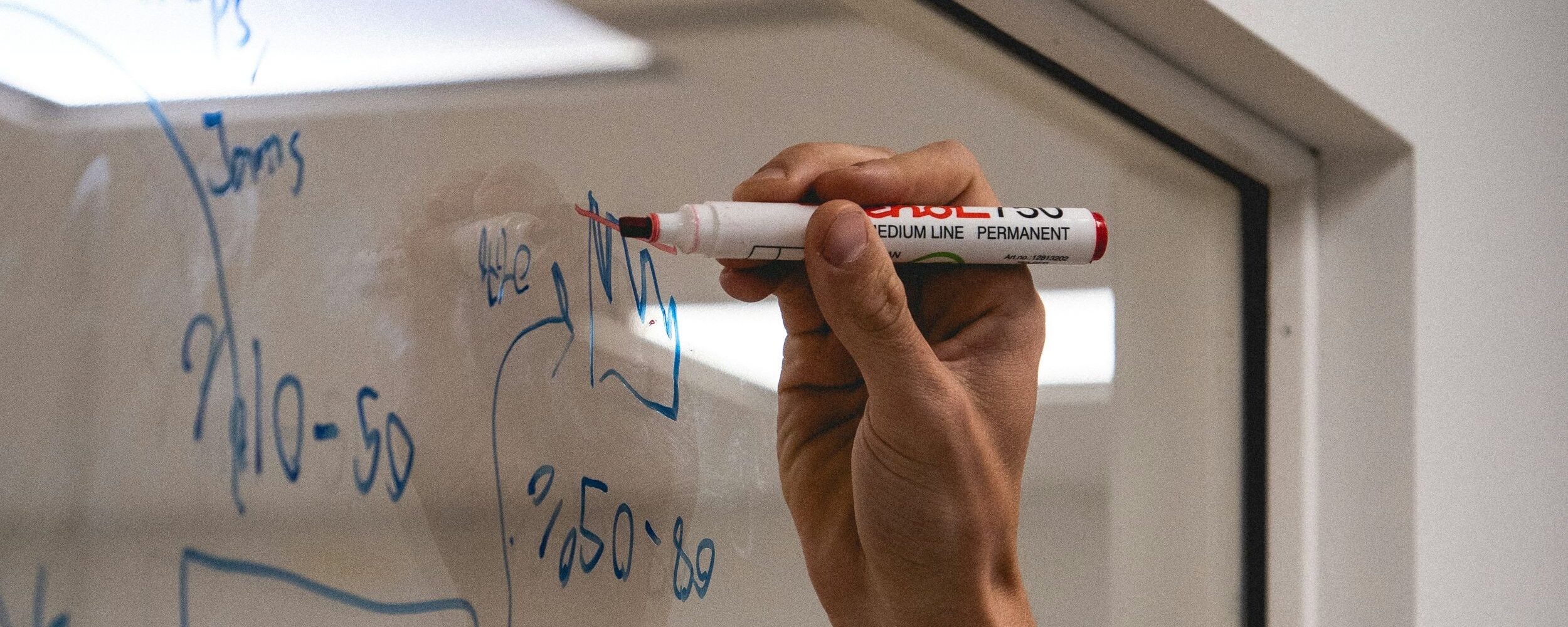 A hand writes formulas on the blackboard.